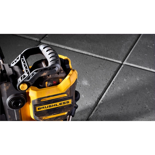 Close-up of a DEWALT brushless power tool with a black handle, shown on a gray tiled floor.