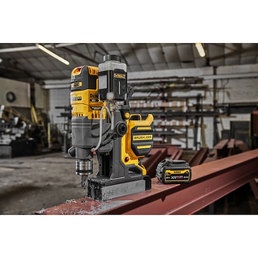 DEWALT brushless magnetic drill and battery on steel beam in an industrial workshop setting.