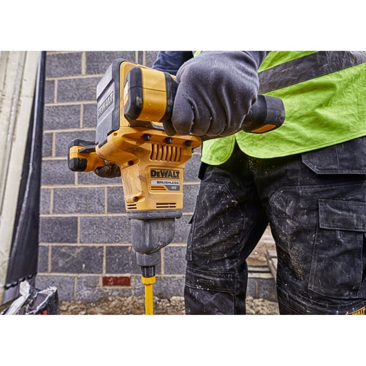 A person wearing gloves is using a DEWALT DCD240X2 brushless power drill to drill into the ground at a construction site.