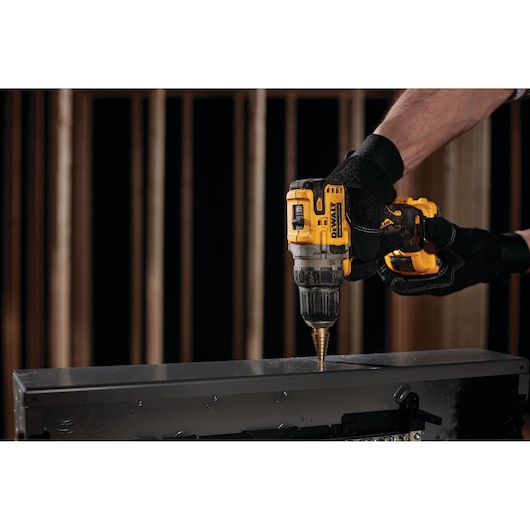 A person wearing black gloves using a yellow DEWALT cordless drill to make a hole in a metal surface.
