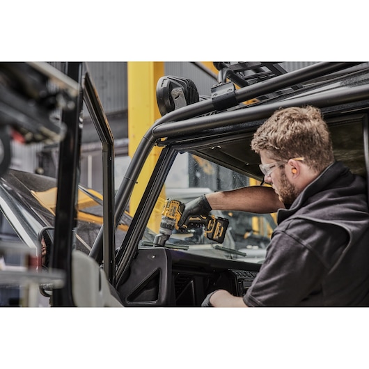 A person using a DEWALT cordless drill inside a vehicle, working on the dashboard area. The person’s face is blurred for privacy.