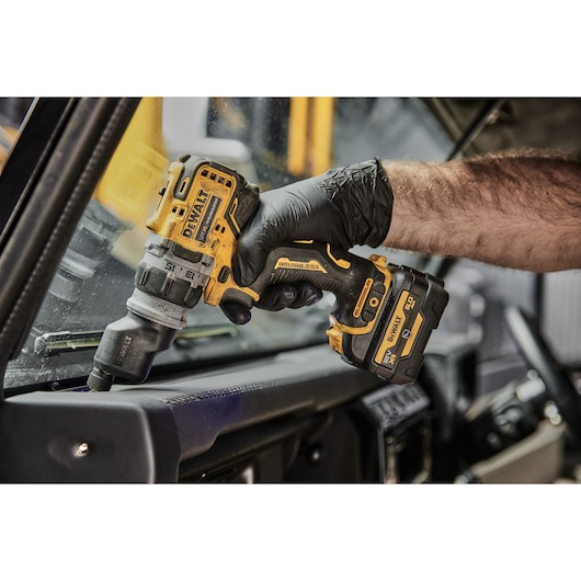 A person wearing a black glove is using a DEWALT cordless drill inside a vehicle, working near the dashboard and windshield.