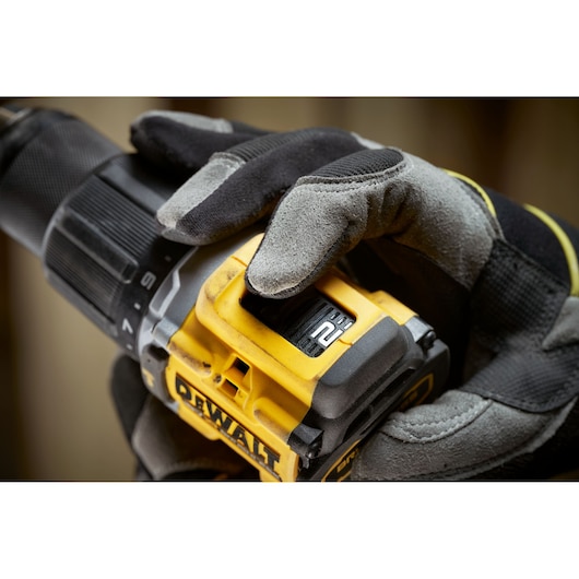 Gloved hand adjusts speed on a yellow DEWALT drill, close-up of controls and branding.
