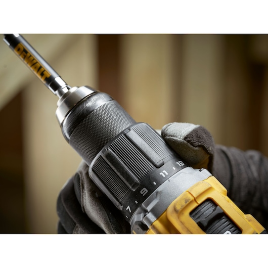Close-up of a DEWALT cordless drill being held with a gloved hand, showing the chuck and adjustment ring.