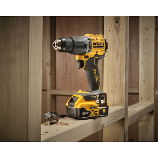 DEWALT cordless drill 18V XR on a wooden beam, shown with a bit and wood shavings in a workshop setting.
