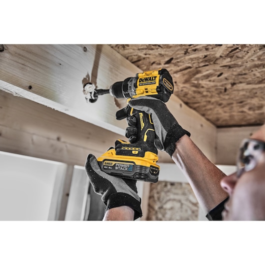 Person uses DEWALT cordless drill to drill into wood beam. The drill features POWERSTACK battery.