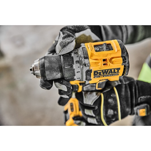 Gloved hands holding a yellow DEWALT cordless drill, close-up view.