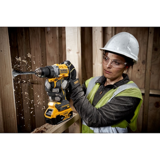 Person drills wood with DEWALT DCD800P2T in construction setting wearing helmet and gloves.