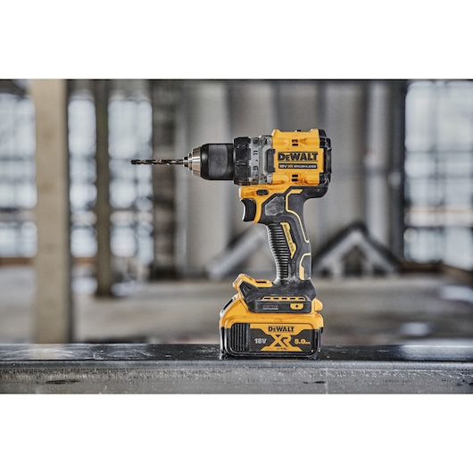 A DEWALT cordless power drill with an attached drill bit, featuring a yellow and black design, is standing upright on a flat surface in an industrial setting.