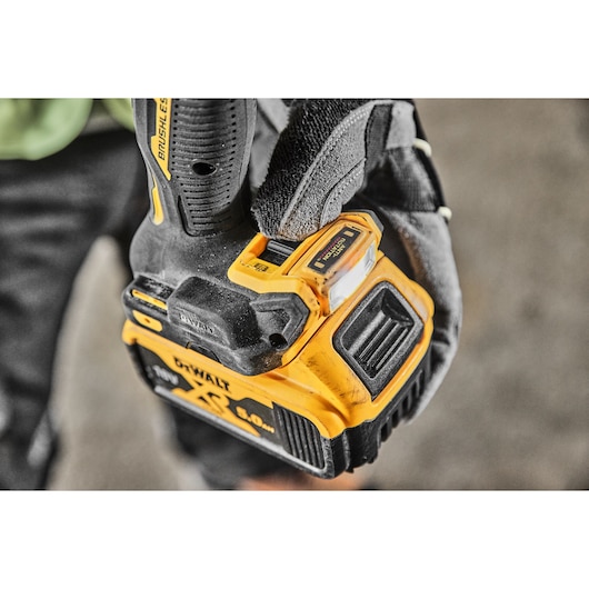 Close-up of a person wearing a work glove holding a yellow and black DEWALT cordless drill with a visible 5.0 Ah XR lithium-ion battery.