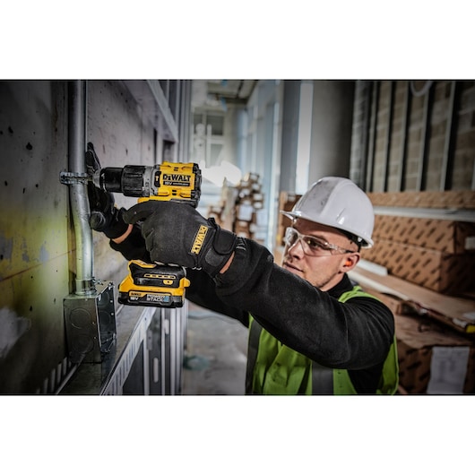 Worker uses a DEWALT DCD805E2T drill on a metal pipe in a construction site while wearing safety gear.