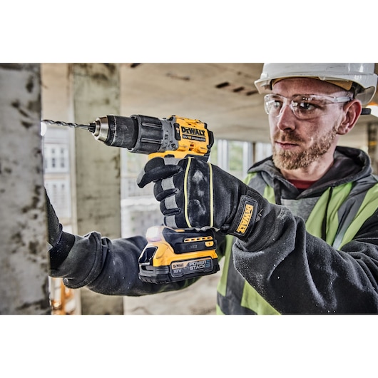 A worker in safety gear uses a DEWALT DCD805E2T 18V cordless drill with a POWERSTACK battery to drill into a metal surface