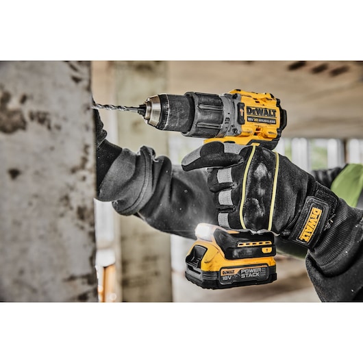 A close-up view of a person using a yellow and black DEWALT cordless drill to make a hole in a metal surface. The person is