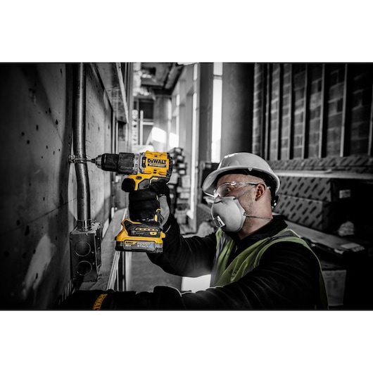 Person using DEWALT DCD805E2T drill on metal pipe at construction site, wearing safety gear.