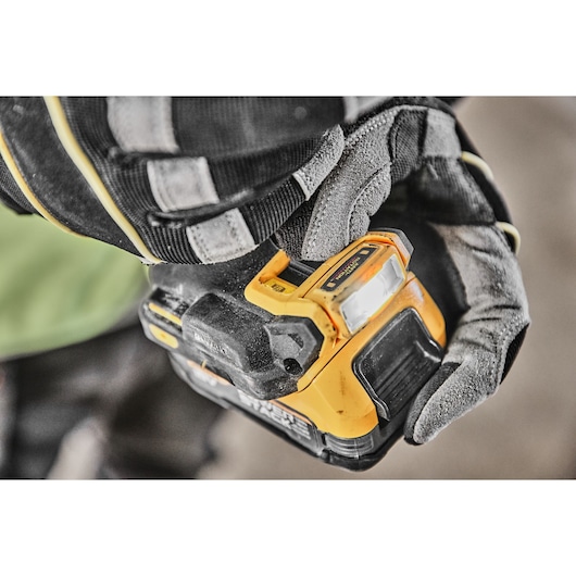 Close-up of a gloved hand holding a DEWALT cordless power tool with a yellow and black design, focusing on the tool's battery and LED work light.