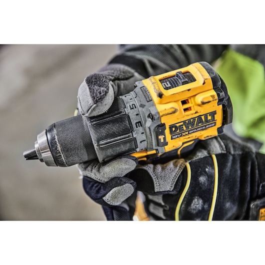 Gloved hand holding a DEWALT 18V XR brushless cordless drill at a worksite.