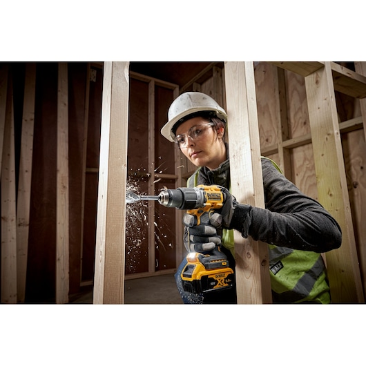 Person using a DEWALT cordless drill to create holes in wooden beams at a construction site.