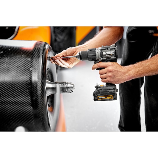 A person uses a DEWALT cordless power drill to work on a car's carbon fiber wheel.