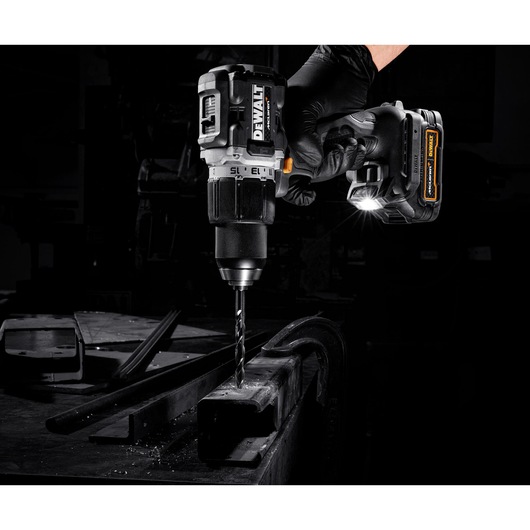A DEWALT cordless drill with a LED light attachment being used to drill into a piece of metal by a gloved hand in a workshop setting.
