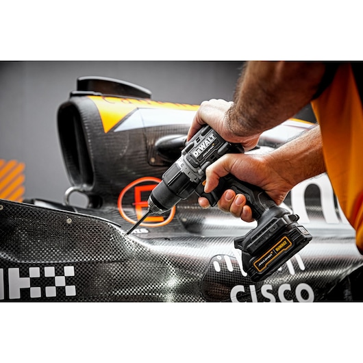 A person using a DEWALT cordless drill (model DCD85ME2GT) to drill into the body of a race car.