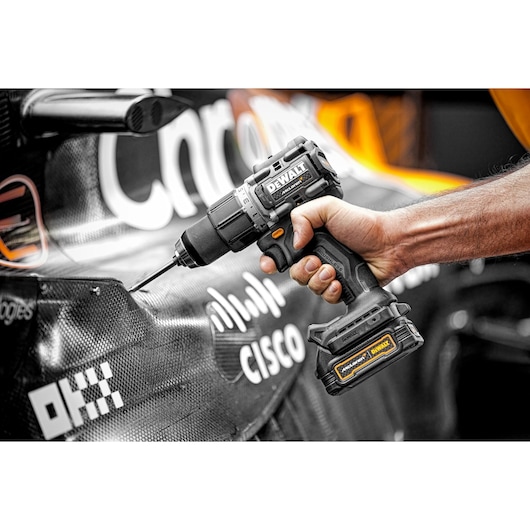 A person using a DEWALT cordless drill to work on a carbon fiber surface of what appears to be a racing car, with visible sponsor logos such as Cisco.