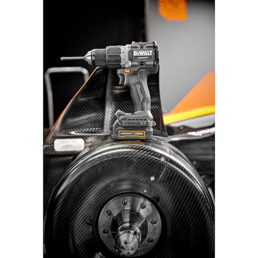 DEWALT cordless drill driver model DCD85ME2GT placed on a carbon fiber automotive part, with a visible yellow and black DEWALT battery attached.