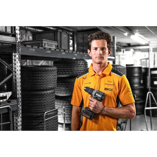 Person in orange shirt holding DEWALT DCD85ME2GT drill in a storage area with tires and shelves.