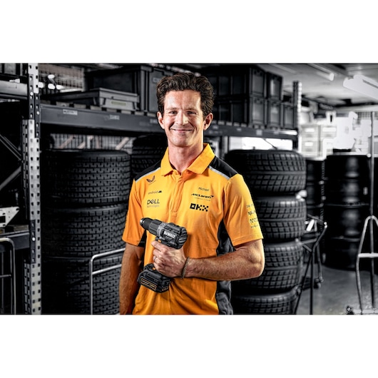 Person with blurred face holding a DEWALT DCD85ME2GT drill in a garage with tires and equipment.