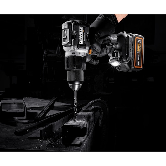 DEWALT cordless drill in use drilling metal with a gloved hand, LED light activated, in a dark workshop setting.