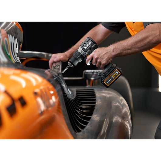 Person using a DEWALT cordless drill on an orange vehicle part.