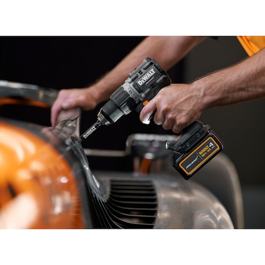 Person uses a DEWALT cordless drill on a metal surface, close-up showing tool detail.