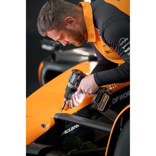 Person using a DEWALT cordless drill on an orange race car's bodywork.