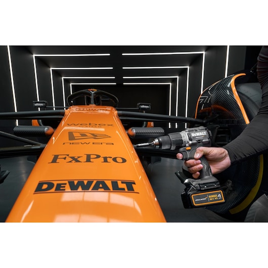 DEWALT drill being used on an orange race car in a modern, illuminated garage setting.