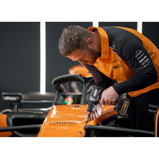 Person uses a DEWALT drill on an orange race car; face is blurred for privacy.