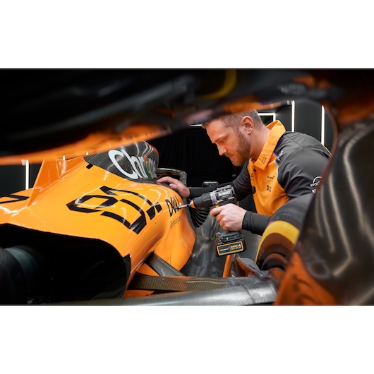 Person uses DEWALT drill on an orange race car, focusing on vehicle maintenance or repair.