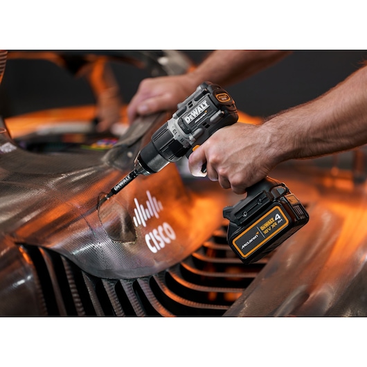 Person using a DEWALT cordless drill on a car part with visible Cisco logo, close-up of hands and tool.