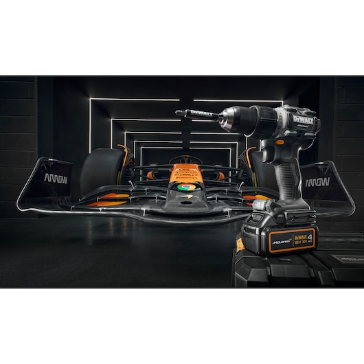 DEWALT power drill on a toolbox with an orange race car in a modern garage background.