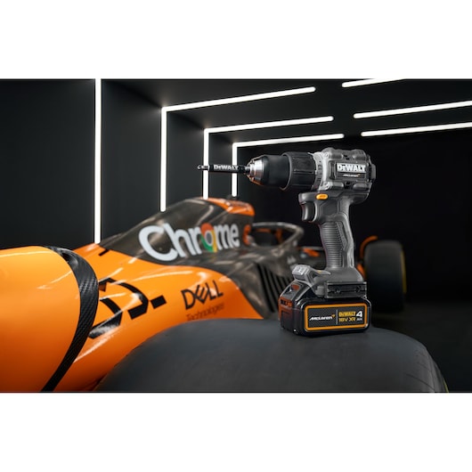 DEWALT cordless drill on a McLaren race car tire in a modern, illuminated garage setting.