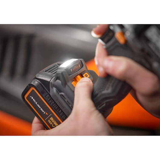 Close-up of hands operating a DEWALT 18V power tool with a lit LED light and McLaren branding visible.