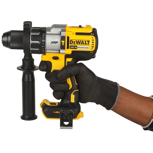 A person wearing a black work glove is holding a yellow and black DEWALT cordless drill with a side handle. The drill is marked with 'XRP', '18V XR', and 'BRUSHLESS'.
