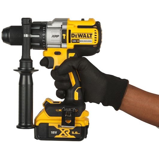 A DEWALT DCD996P2 18V XR Brushless cordless drill with a side handle, being held by a gloved hand.