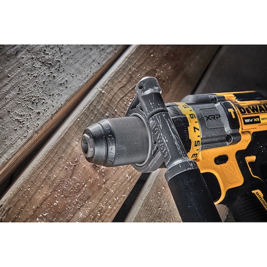 Close-up of a DEWALT DCD999H2T cordless drill in use, with wood shavings on a wooden plank surface.