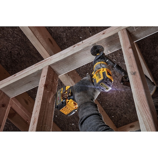 DEWALT DCD999NT drill in use, boring a hole through wooden beams by a gloved hand in a construction setting.