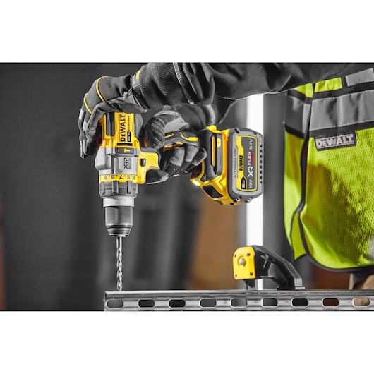 Worker uses DEWALT cordless drill to drill into metal, wearing gloves and safety vest on a construction site.