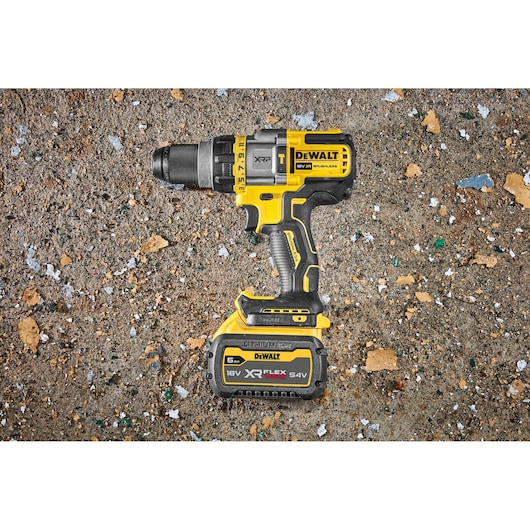 A DEWALT cordless power drill, model DCD999NT, with a yellow and black design, placed on a rough concrete surface. The drill is equipped with an XR FLEXVOLT 18V/54V lithium-ion battery.