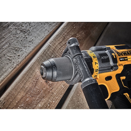 Close-up of a DEWALT cordless drill with a side handle, shown on a wooden surface with sawdust.