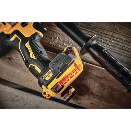 Close-up view of a DEWALT brushless cordless drill, showing the handle, battery attachment area, and a side handle grip, placed on wooden boards.