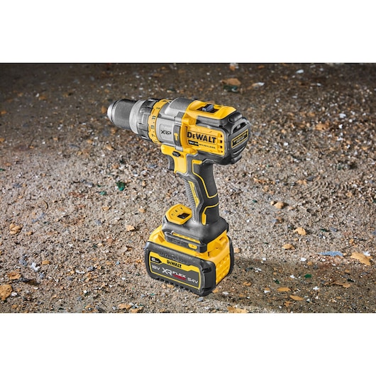 A DEWALT cordless power drill with a yellow and black body, standing upright on a rough surface. The drill features XR FLEXVOLT technology and an 18V battery pack attached at the base.