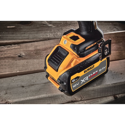 Close-up of a DEWALT XR FLEXVOLT 18V/54V battery attached to a tool resting on wooden planks.