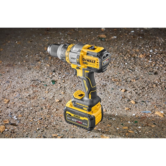 DEWALT DCD999X1 cordless drill with 18V XR FLEXVOLT battery, standing on rough ground.
